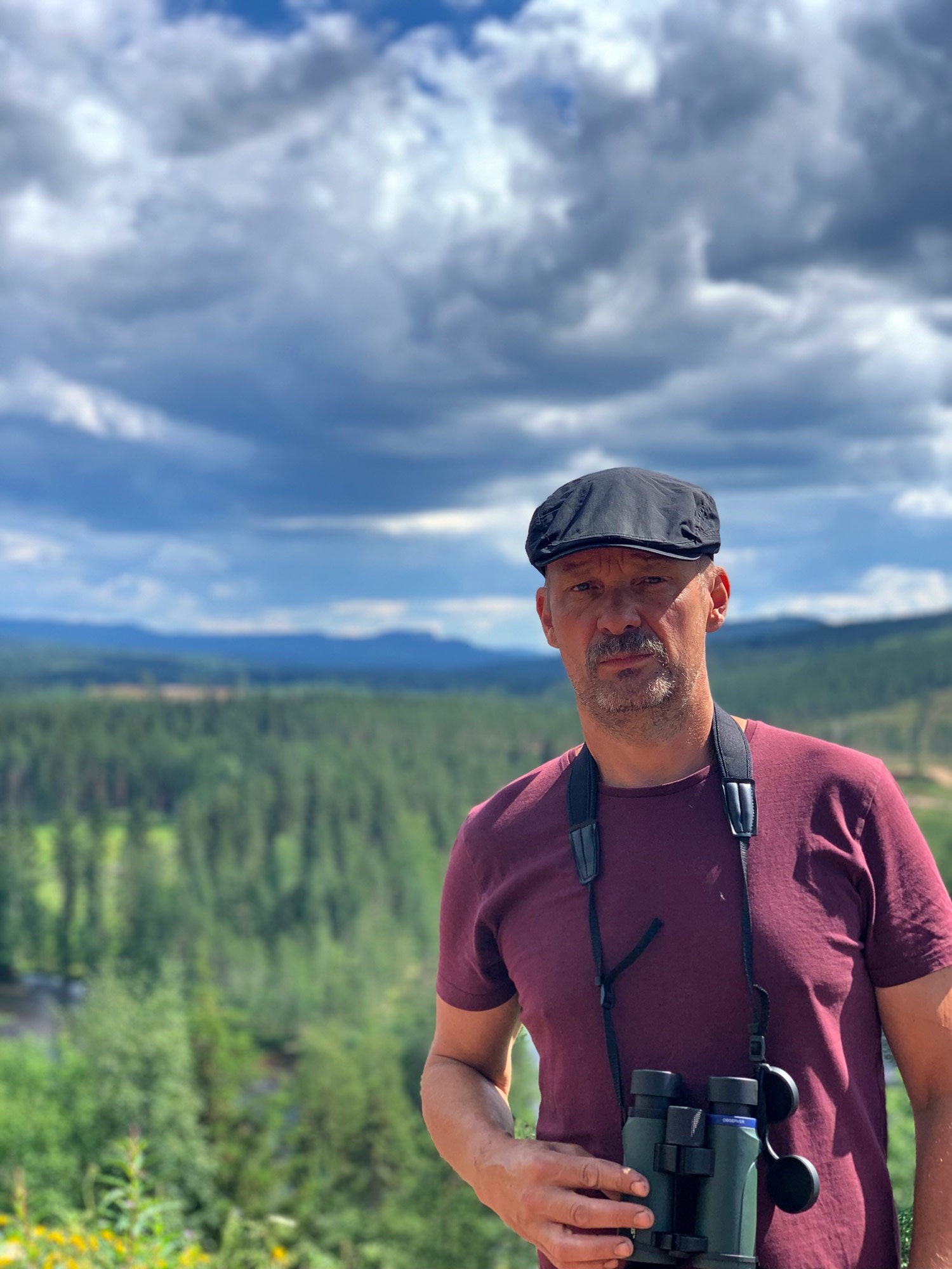 Peter med en kikare runt halsen med skog och berg i bakgrunden